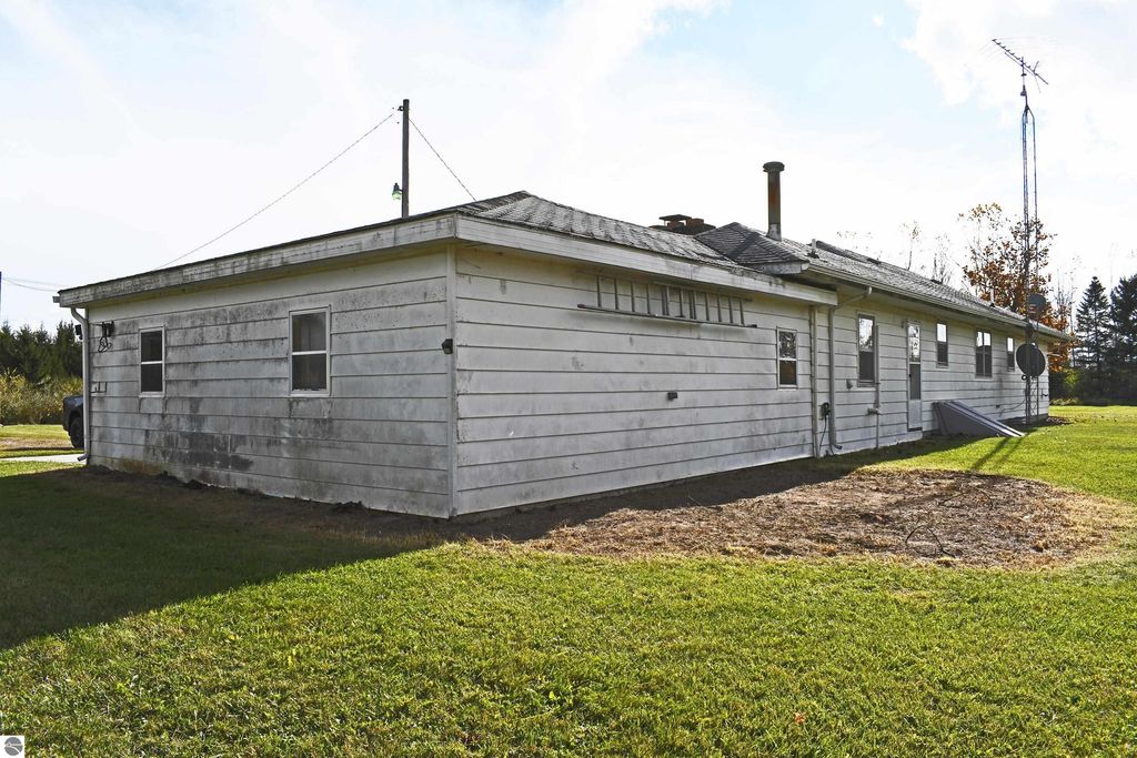 Ranch-style home exterior at 2275 Noble Road, Tawas City, with a grassy yard, weathered white siding, and nearby utility poles, showcasing a secluded property on 40 acres.