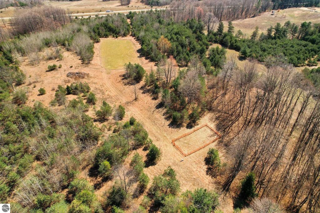 Aerial view of a 7.63-acre wooded parcel in Manton, MI, featuring a cleared area suitable for building, surrounded by trees and natural landscape, ideal for outdoor retreat or hunting getaway.