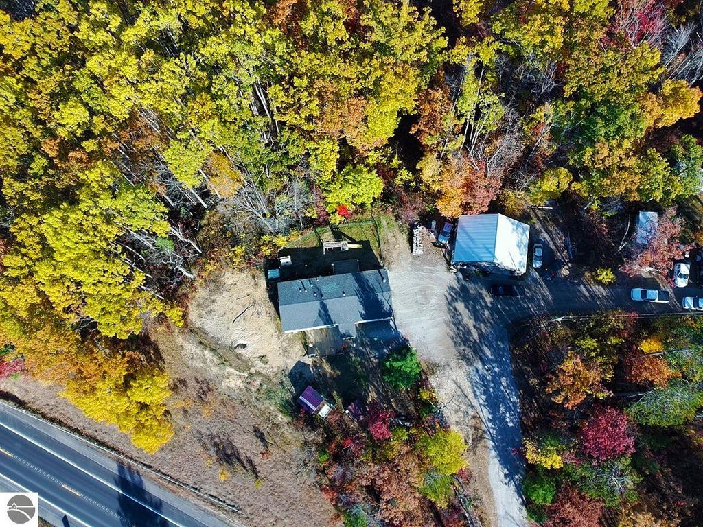 Aerial view of a cozy home surrounded by vibrant autumn foliage on 5.23 acres in Rose City, MI, featuring a partially finished pole barn and nearby road access.