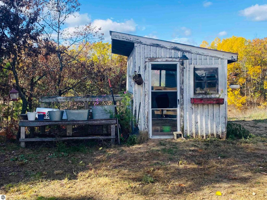Wooden shed with a porch, surrounded by trees, featuring gardening supplies and a serene natural setting, located on 5.23 acres near Rose City, MI.