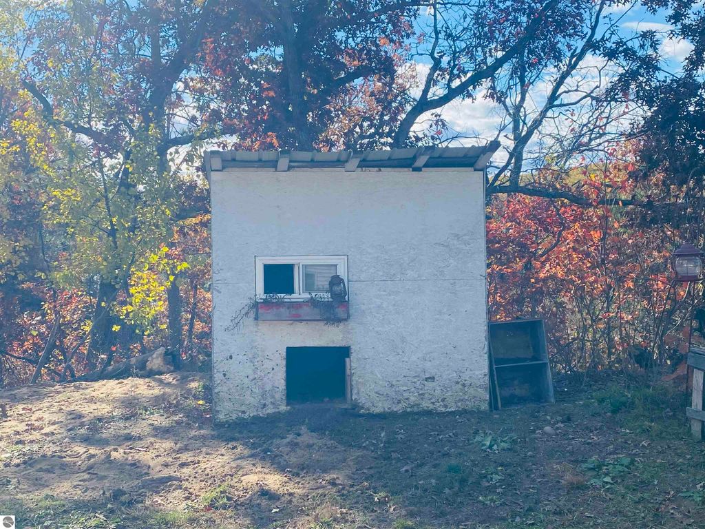 Small white outbuilding with a window and door, surrounded by colorful autumn foliage, on a property for sale in Rose City, MI, featuring 5.23 acres of land.