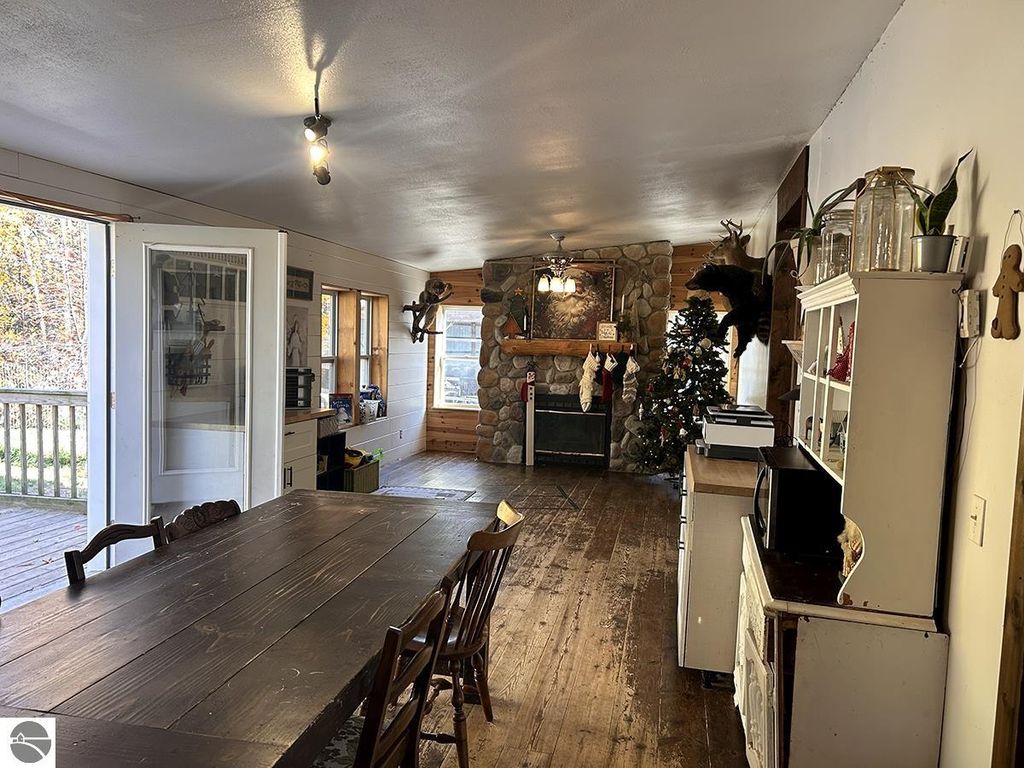 Cozy interior of a rustic home featuring a large wooden dining table, stone fireplace, decorated Christmas tree, and natural light from windows, set in a serene Up North retreat in Rose City, MI.