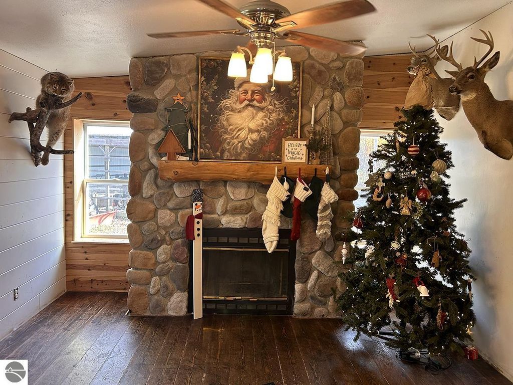 Cozy living room with stone fireplace, Christmas tree, holiday decorations, and mounted deer heads, reflecting a rustic Up North retreat atmosphere.