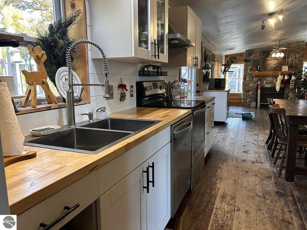 Modern kitchen with stainless steel appliances, wooden countertops, and rustic decor, featuring a view of a cozy dining area and a stone fireplace, ideal for a northern retreat.