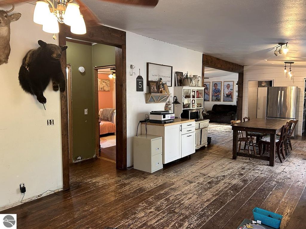 Interior view of a rustic home featuring wooden floors, a bear and deer mount on the wall, a kitchen area with white cabinetry, and a dining table, emphasizing the cozy Up North retreat atmosphere.