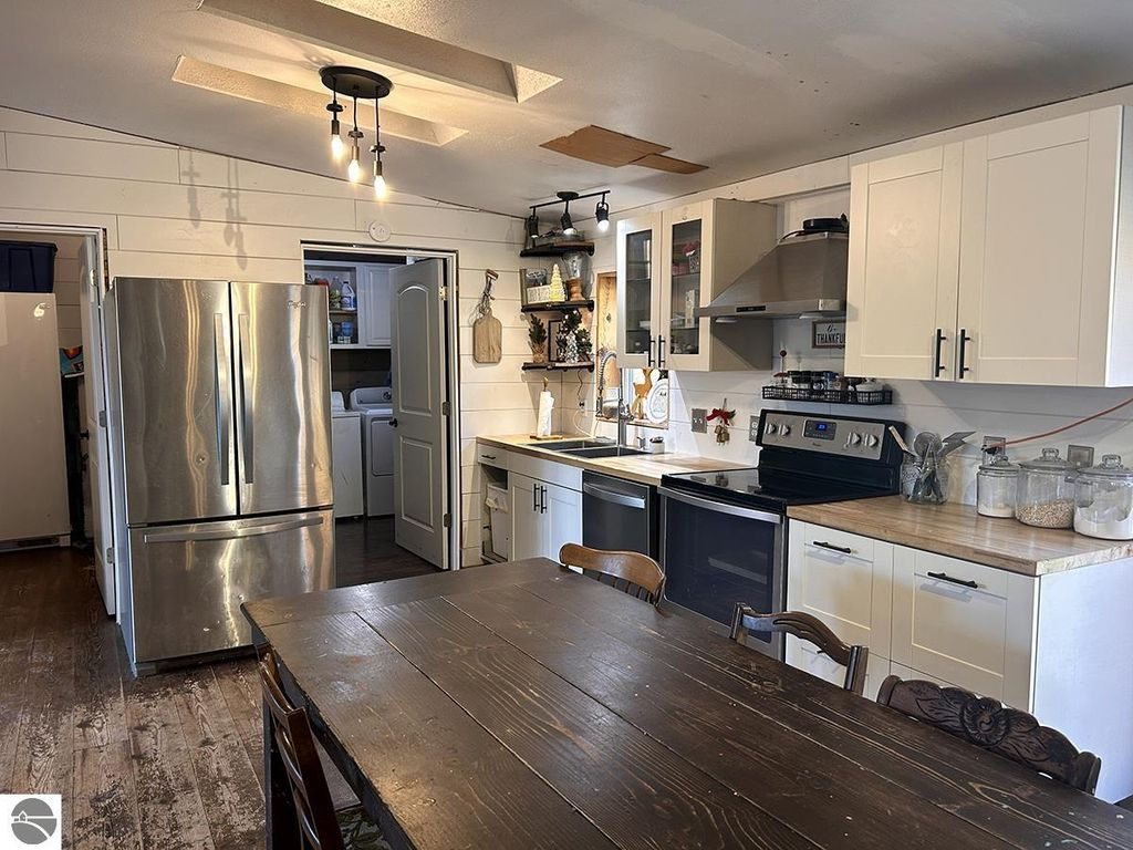 Modern kitchen interior with stainless steel appliances, wooden dining table, and white cabinetry, showcasing a cozy Up North retreat atmosphere in Rose City, MI.