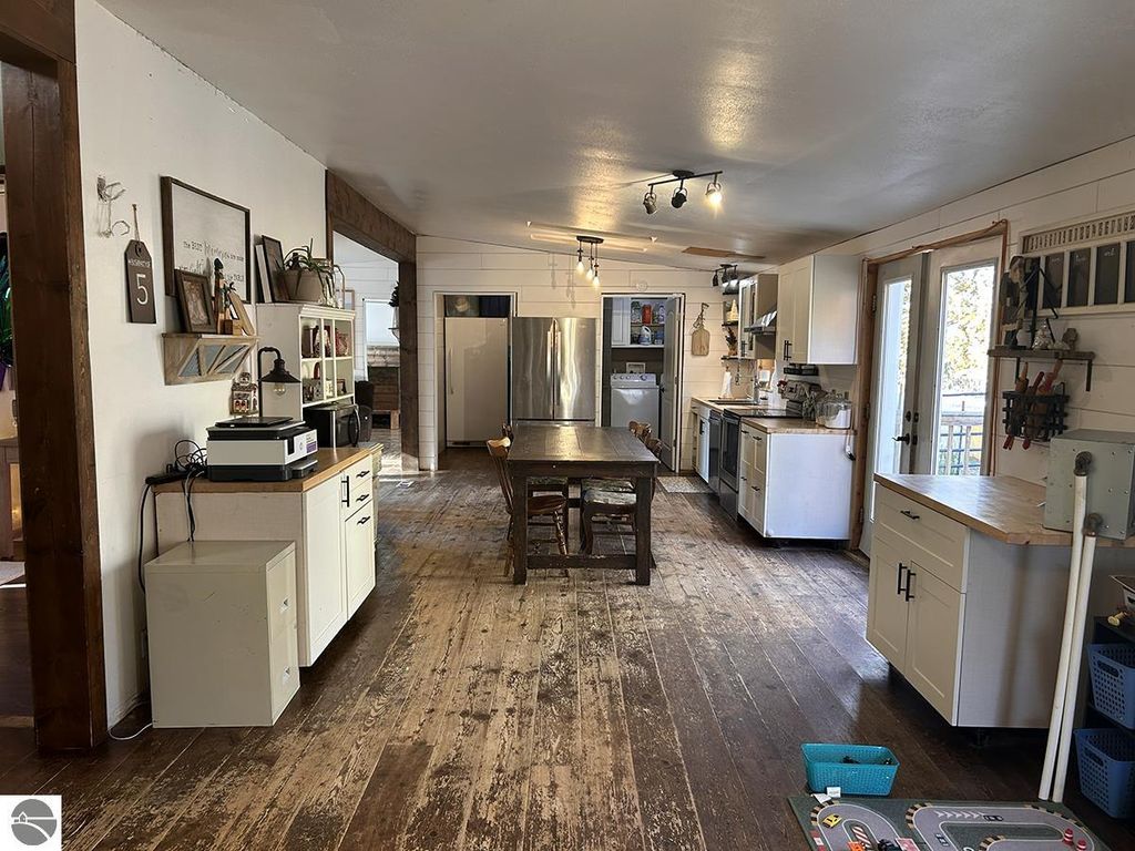 Cozy kitchen interior with wooden flooring, featuring white cabinets, stainless steel appliances, a large dining table, and a view of the outdoors through French doors, highlighting the rustic charm of the home at 5885 S Mt Tom Road, Rose City, MI.
