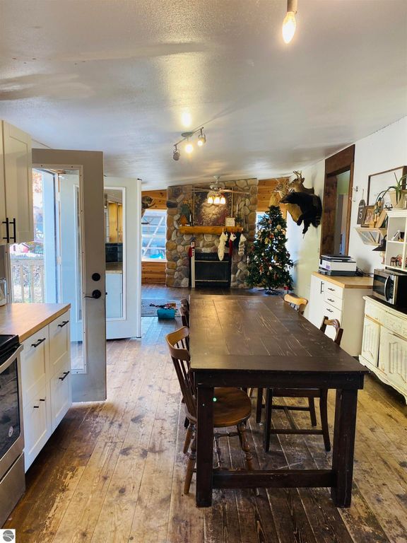 Cozy kitchen interior featuring a wooden dining table, stone fireplace, decorated Christmas tree, and rustic decor, highlighting the inviting atmosphere of the 3-bedroom home on 5.23 acres in Rose City, MI.