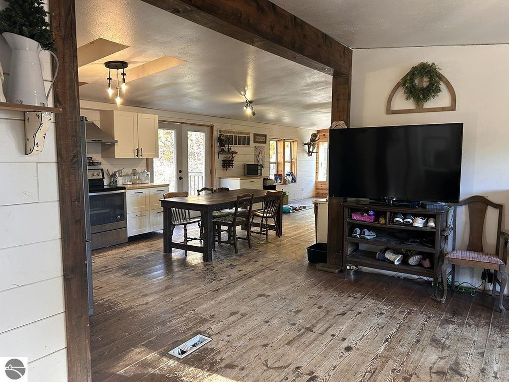 Cozy interior of a 3-bedroom, 2-bath home for sale in Rose City, MI, featuring a dining area, kitchen with modern appliances, and living space with a large TV, highlighting rustic wooden floors and natural light.