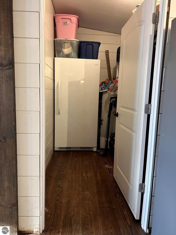 Interior storage area featuring a white refrigerator, stacked plastic bins, and wooden flooring, illustrating the home's potential for organization and utility.