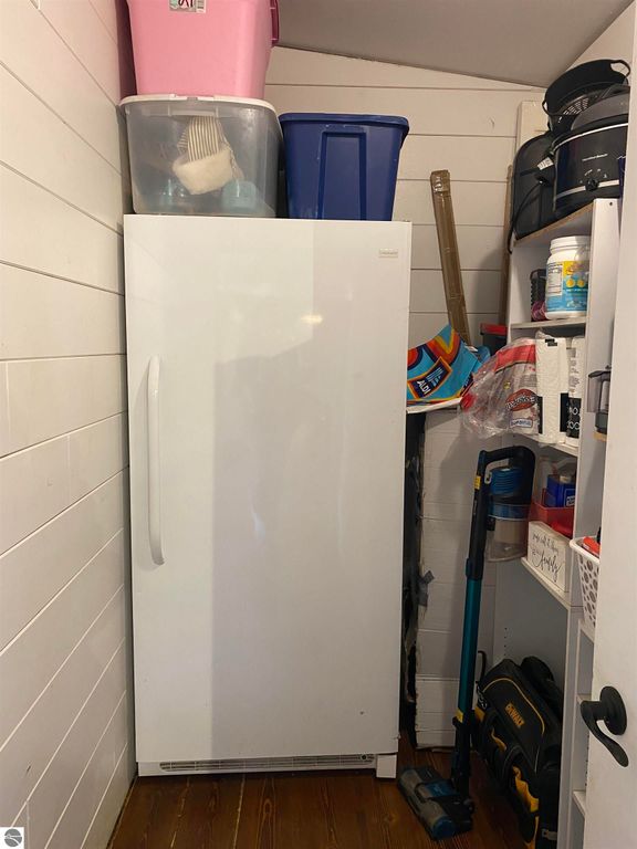 Storage area featuring a white refrigerator alongside various containers and cleaning supplies, showcasing organization within a home setting.