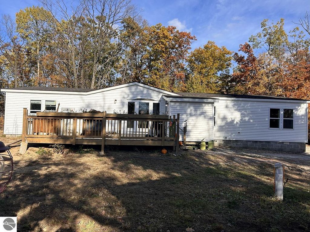 Cozy home at 5885 S Mt Tom Road, Rose City, MI, featuring a wooden deck, surrounded by autumn foliage, ideal for outdoor enthusiasts and privacy seekers.