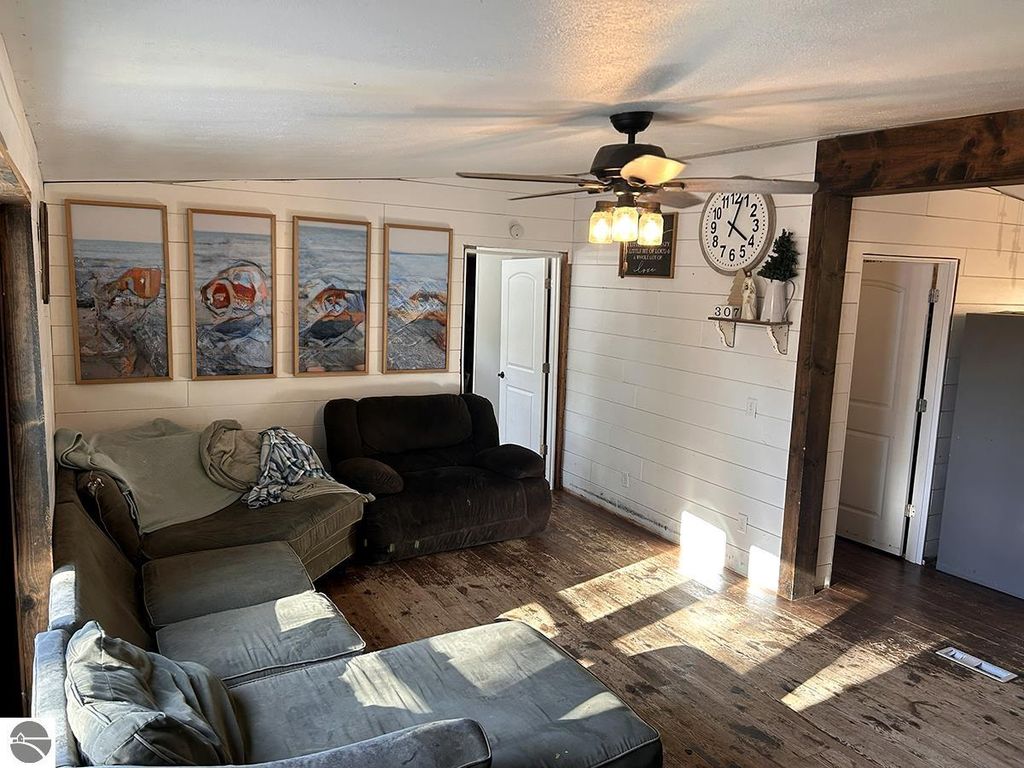 Cozy living room featuring a sectional sofa, wall art of lakeside scenes, ceiling fan, and wooden accents, highlighting the inviting atmosphere of a 3-bedroom home in Rose City, MI.