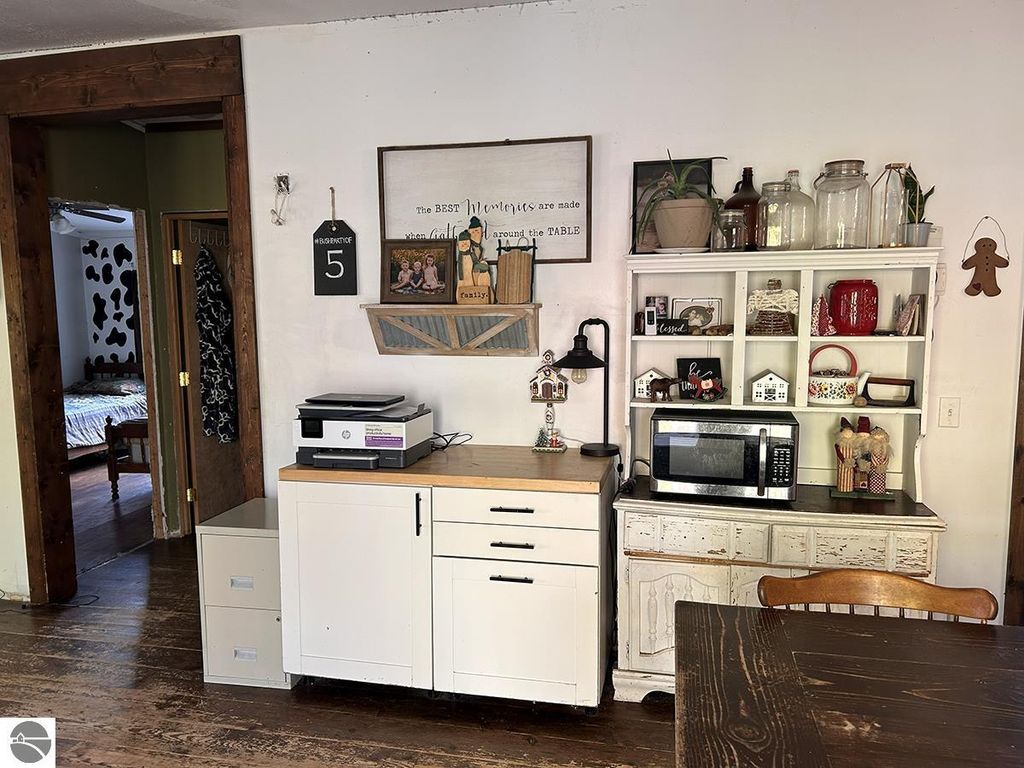 Cozy kitchen interior featuring a white cabinet, microwave, and decorative items, with a view of a bedroom in the background, reflecting a rustic Up North retreat atmosphere in Rose City, MI.