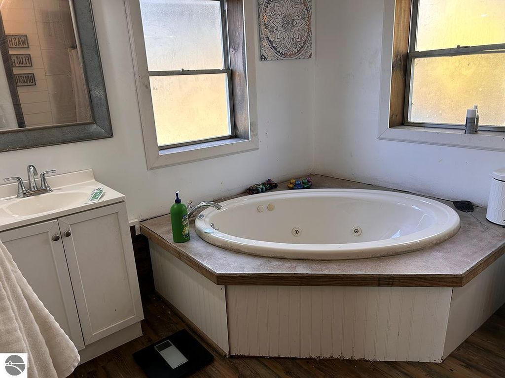 Bathroom interior featuring a corner jacuzzi tub, white cabinetry with sink, and large windows providing natural light, set in a cozy home environment.