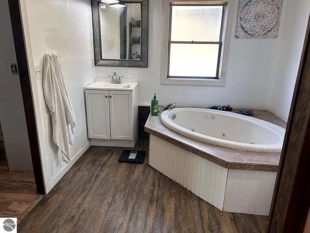 Bathroom interior featuring a white jacuzzi tub, sink with mirror, and wooden flooring, showcasing a cozy and rustic aesthetic suitable for a home retreat in Rose City, MI.