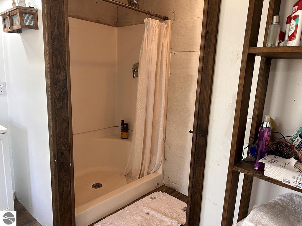 Shower area in a bathroom featuring a white tub, beige curtain, and wooden accents, showcasing a cozy Up North retreat at 5885 S Mt Tom Road, Rose City, MI.