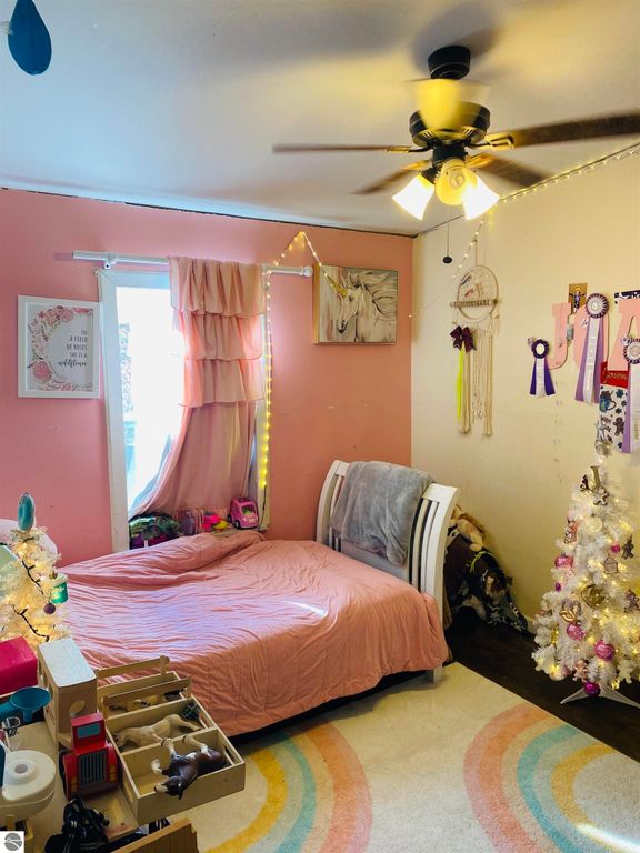 Cozy bedroom with pink walls, a white bedspread, decorative fairy lights, and a small white Christmas tree, showcasing a warm and inviting atmosphere.