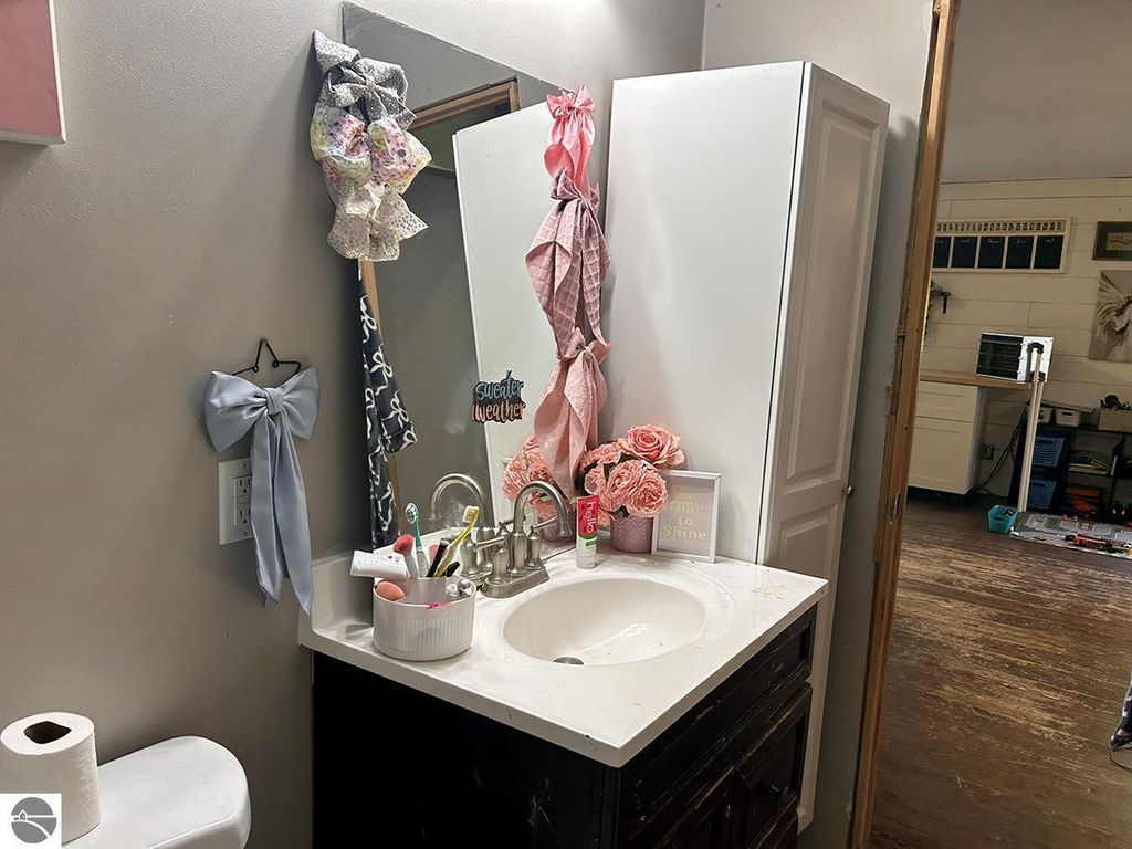 Bathroom vanity with a sink, decorative flowers, and hair accessories, showcasing a cozy Up North retreat aesthetic in a home for sale in Rose City, MI.