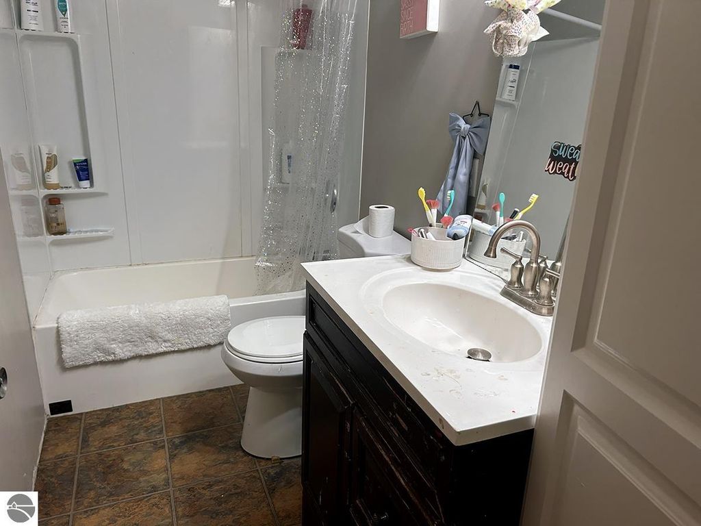 Bathroom featuring a white bathtub, shower curtain, dark wood vanity with sink, and various toiletries on the counter, reflecting a cozy, lived-in atmosphere in a home for sale at 5885 S Mt Tom Road, Rose City, MI.