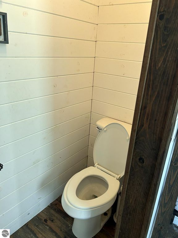 Bathroom interior featuring a white toilet against shiplap walls and rustic wood flooring, part of a cozy home listing in Rose City, MI.