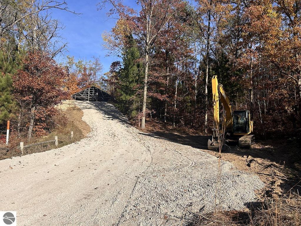 Gravel driveway leading to a partially constructed pole barn surrounded by autumn foliage and an excavator, highlighting the outdoor space of the property at 5885 S Mt Tom Road, Rose City, MI.