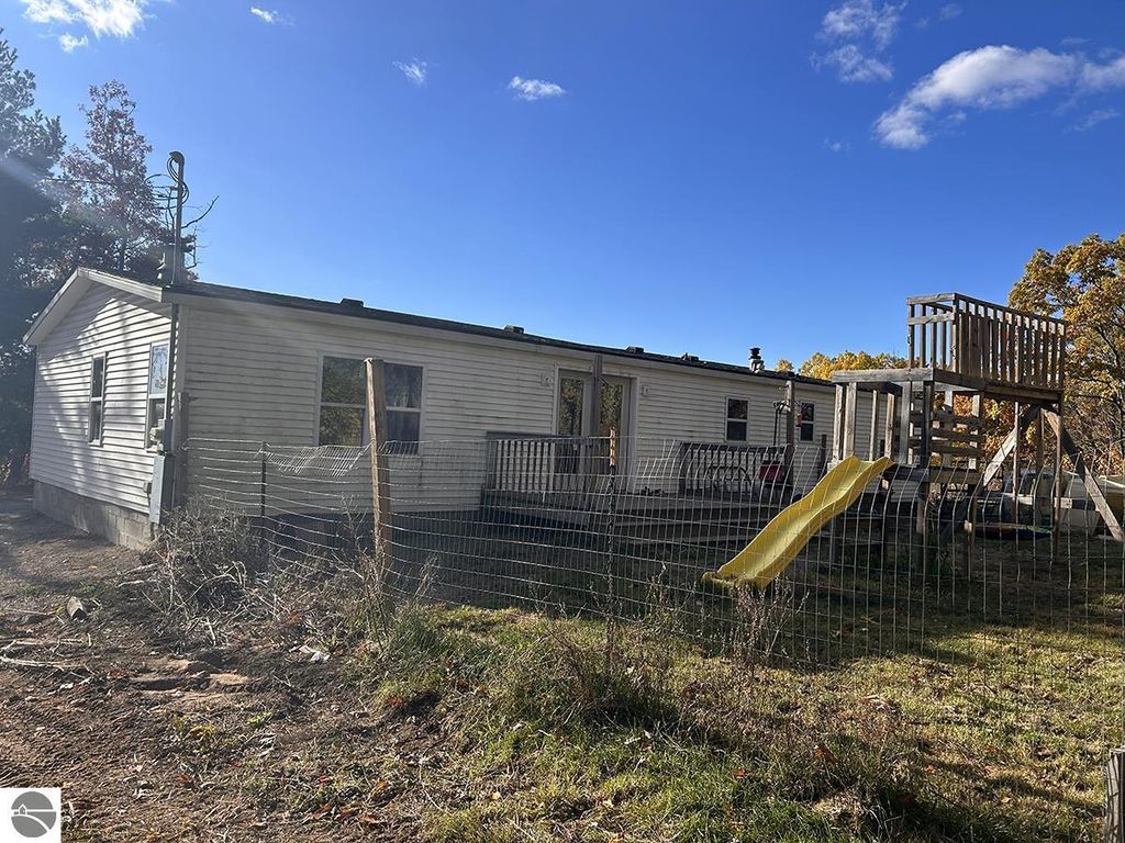 Cozy 3-bedroom, 2-bath home on 5.23 acres in Rose City, MI, featuring a fenced yard, wooden deck with slide, and surrounded by mature trees.