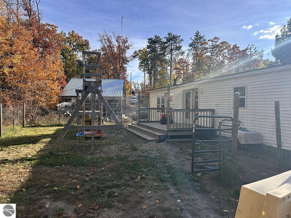 Cozy outdoor view of a 3-bedroom home in Rose City, MI, featuring a wooden play structure, fenced yard, and mature trees, highlighting the property's spacious 5.23 acres and nearby recreational opportunities.
