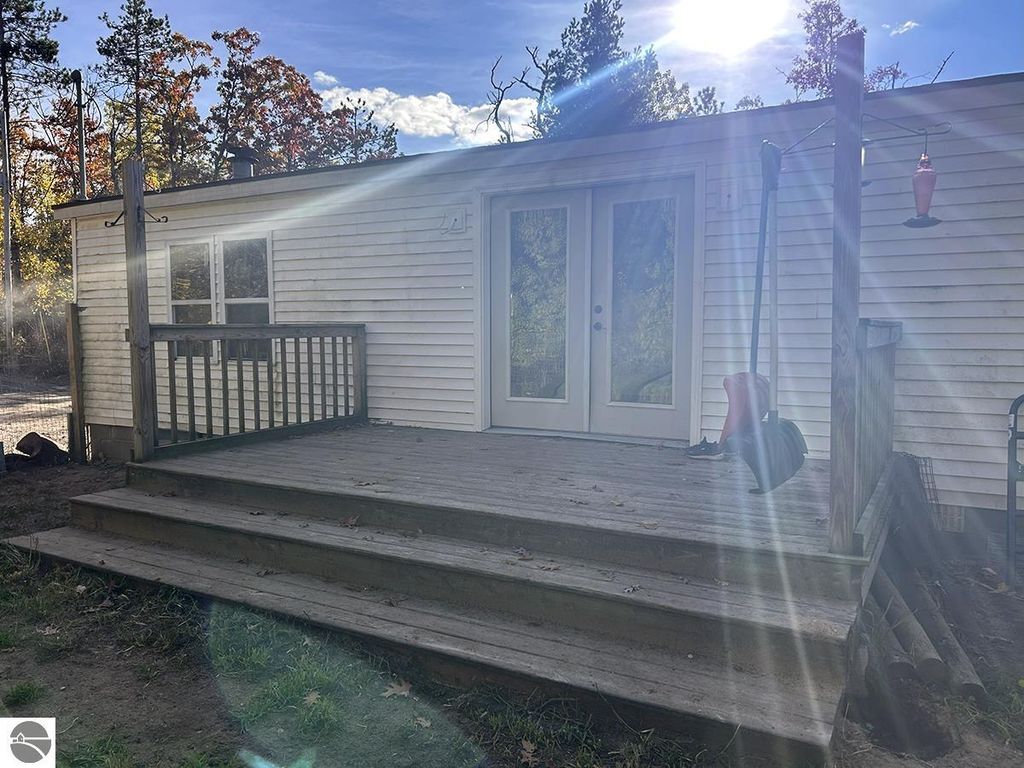 Cozy home exterior featuring a wooden deck, double doors, and surrounding trees, ideal for a retreat on 5.23 acres in Rose City, MI.