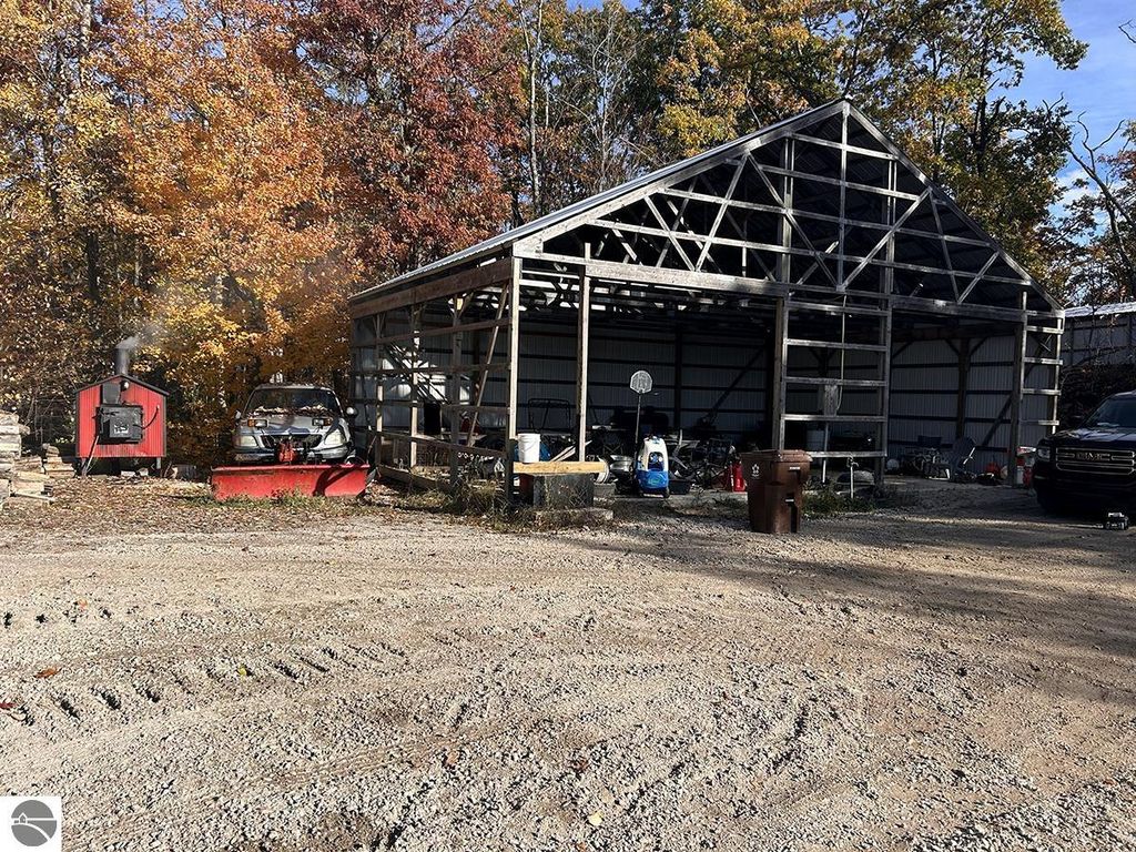Partially finished 30x40 pole barn with a steel roof and cement floor, surrounded by trees and gravel driveway, showcasing outdoor storage potential near 5885 S Mt Tom Road, Rose City, MI.