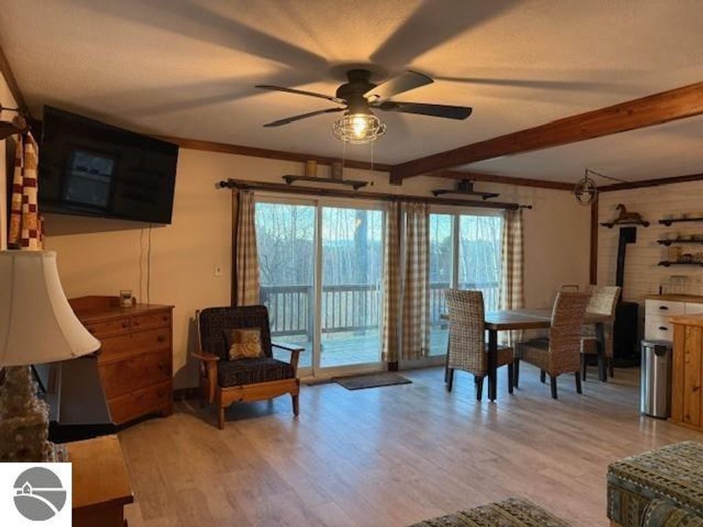 Chalet-style living room with natural light, featuring a TV, wooden furniture, and a dining area, overlooking a deck with serene views, ideal for year-round living near Torch Lake.