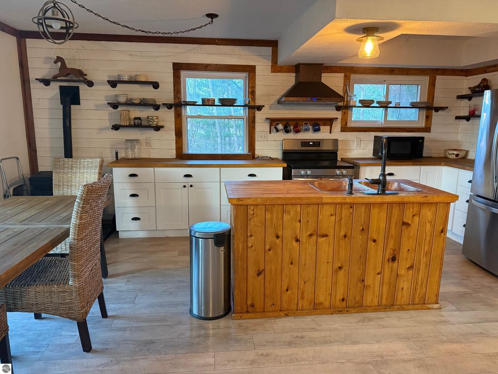 Chalet-style kitchen featuring wooden island, modern appliances, and rustic decor, showcasing a cozy living space in Alden, MI home for sale.