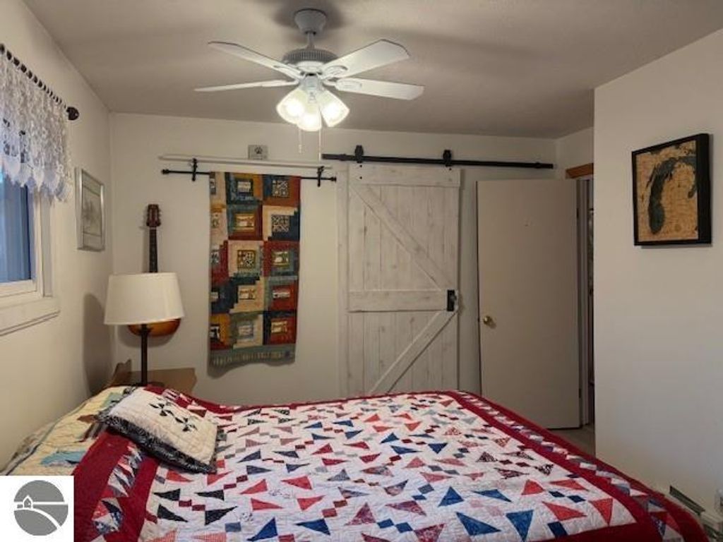 Chalet-style bedroom featuring a patterned quilt, ceiling fan, and barn-style door, with a cozy and inviting atmosphere in a home near Torch Lake, Alden, MI.