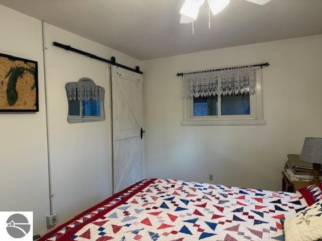 Chalet-style bedroom featuring a quilted bedspread, rustic sliding barn door, and wall decor including a map of Michigan, set in a cozy, natural ambiance.