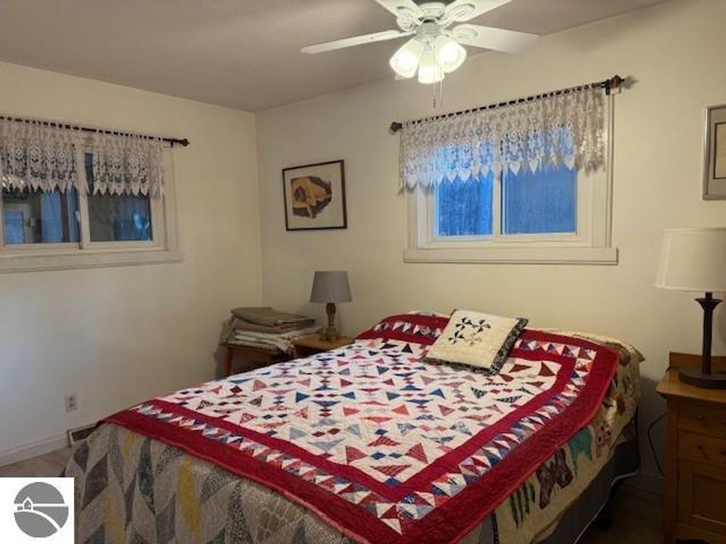 Chalet-style bedroom featuring a quilted bedspread, window with lace curtains, and bedside table with lamp, set in a cozy interior.