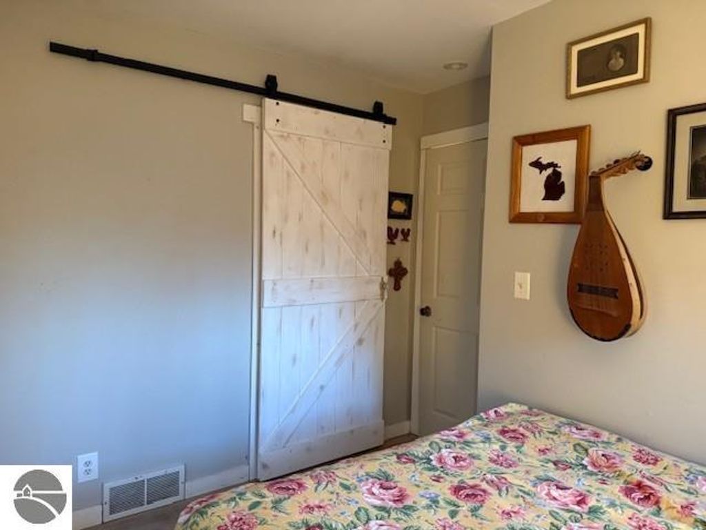 Chalet-style bedroom featuring a floral-patterned bedspread, a sliding barn door, and rustic decor including framed art and a stringed instrument, reflecting a cozy ambiance in a home near Torch Lake.
