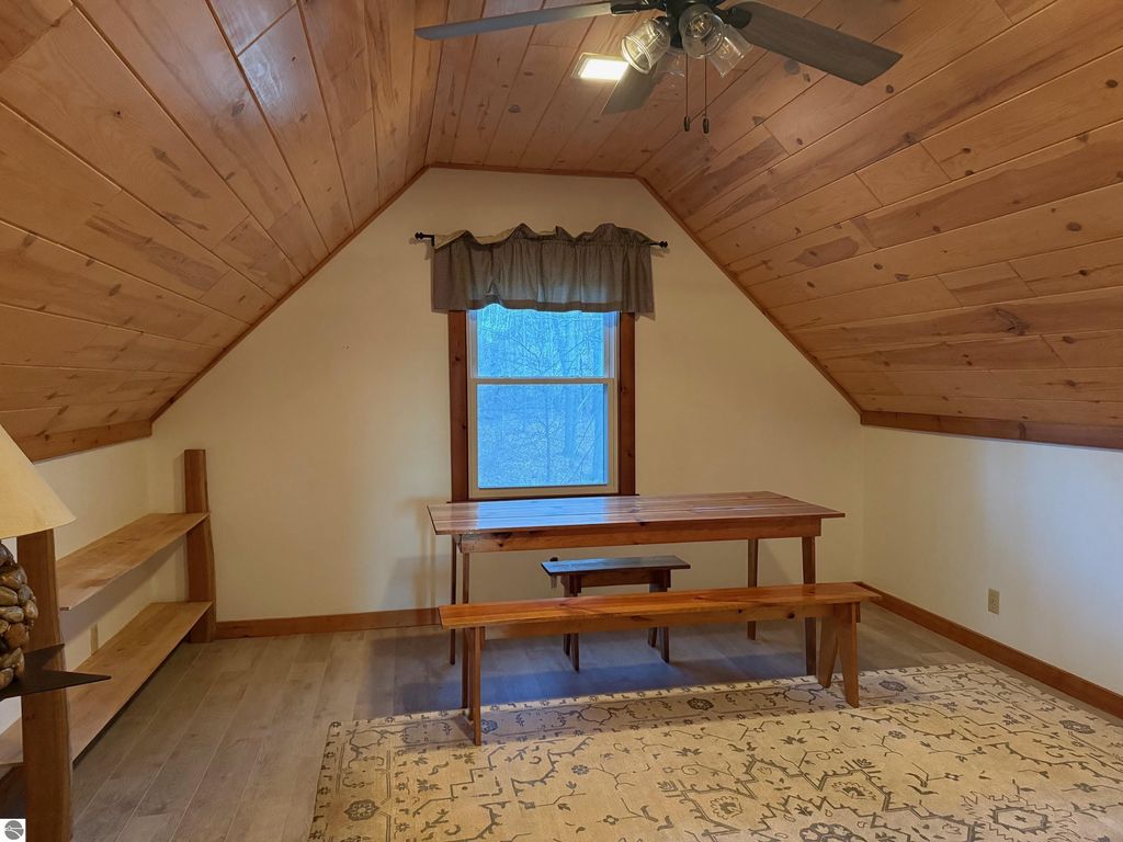 Chalet-style interior featuring wooden paneling, a dining table with benches, and a window view, highlighting the cozy atmosphere of the property at 9535 Serenity Trail, Alden, MI.