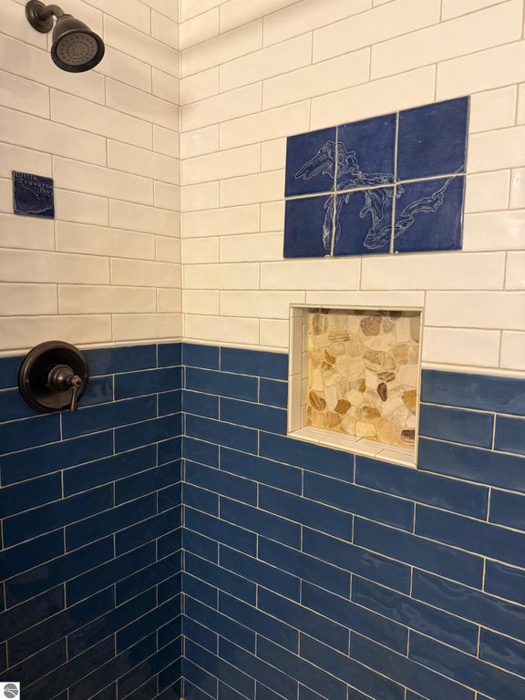 Chalet-style bathroom shower featuring blue and white tile design, decorative Great Lakes map tile, and stone accent niche.