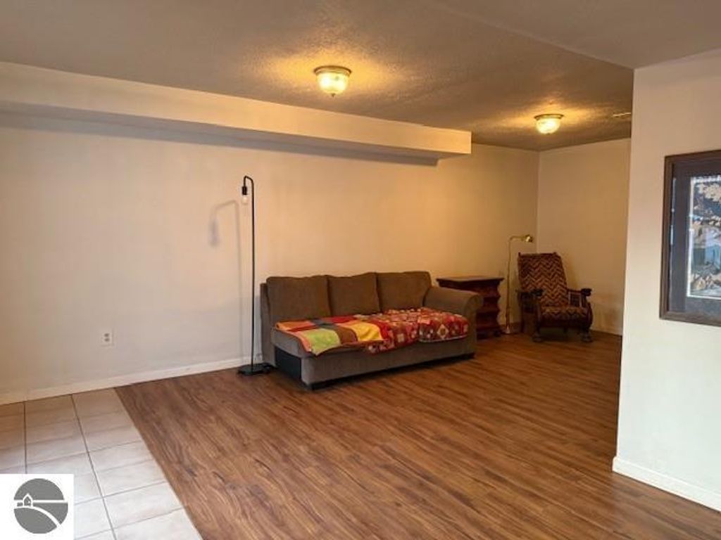 Spacious living area in updated chalet home at 9535 Serenity Trail, featuring a comfortable couch with a colorful throw, wood flooring, and natural light, ideal for relaxing in a peaceful setting near Torch Lake.