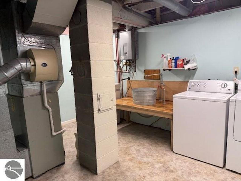 Basement laundry area featuring a washing machine, utility sink, and heating system, showcasing functional space in the chalet-style home at 9535 Serenity Trail, Alden, MI.