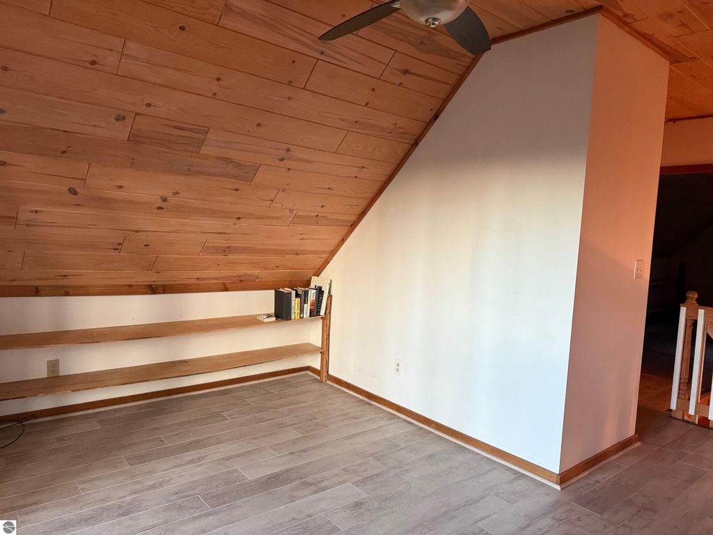 Chalet-style interior featuring sloped wooden ceiling, light-colored walls, and open shelving with books, showcasing a warm and inviting space in a home for sale in Alden, MI.