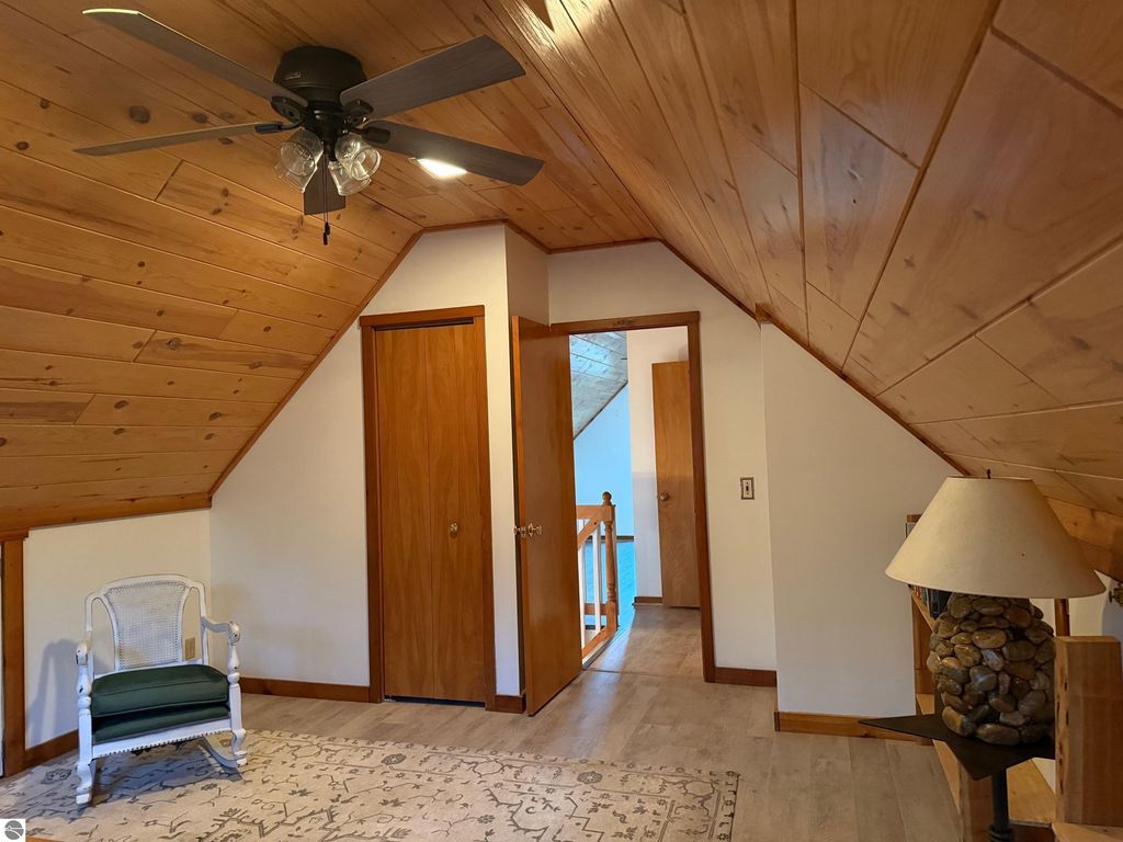 Chalet-style interior featuring wooden ceiling, ceiling fan, cozy chair, and doorway leading to additional rooms in a serene setting at 9535 Serenity Trail, Alden, MI.