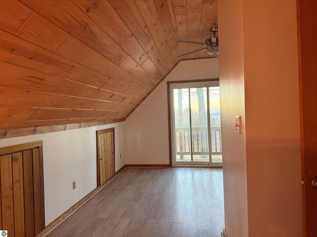 Chalet-style interior with wood-paneled ceiling, wooden floors, and sliding glass doors leading to a scenic view, highlighting the cozy atmosphere of the property at 9535 Serenity Trail, Alden, MI.