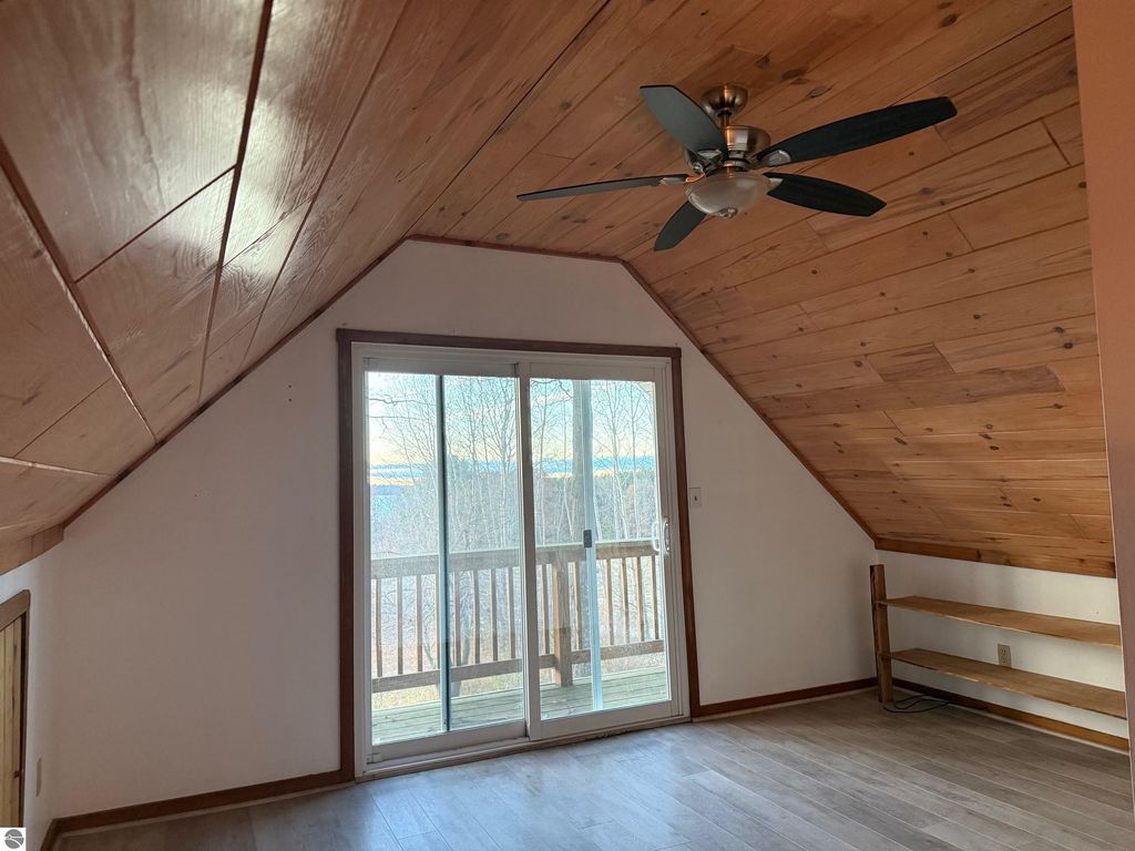 Chalet-style interior with wooden ceiling, ceiling fan, and sliding glass door leading to a deck with views of the natural surroundings near Torch Lake, part of the property listing at 9535 Serenity Trail, Alden, MI.