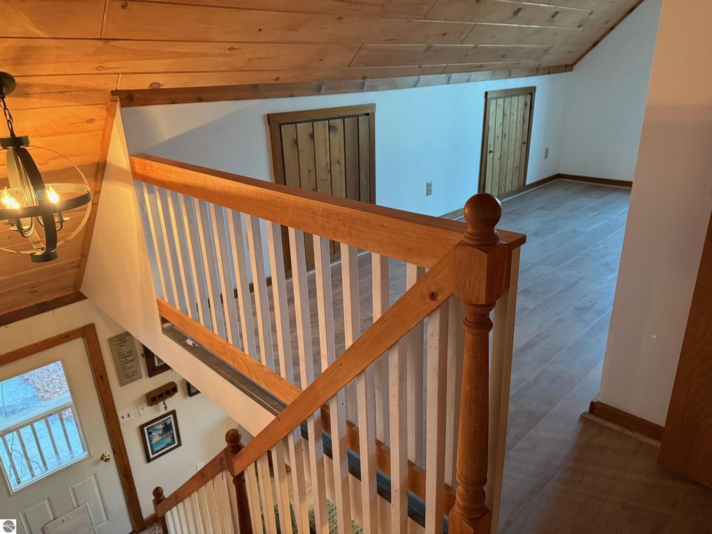 Chalet interior showcasing wooden staircase, vaulted ceiling, and open space leading to additional rooms in the updated home at 9535 Serenity Trail, Alden, MI.