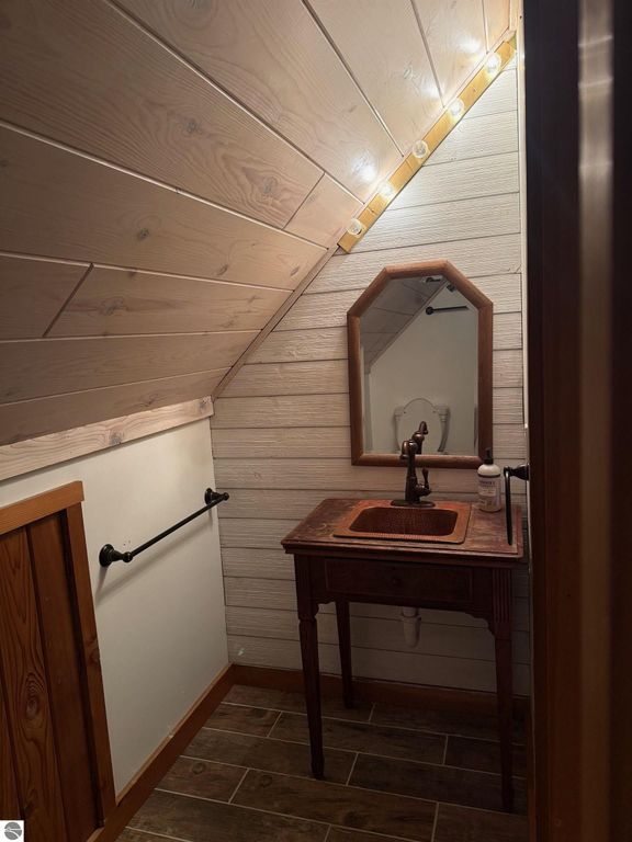 Chalet-style bathroom featuring rustic wooden accents, an octagonal mirror, and a vintage sink, illuminated by warm overhead lights, emphasizing a cozy, updated design in a home near Torch Lake.