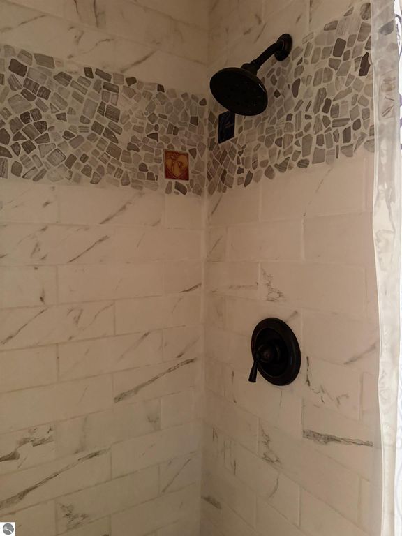 Shower interior featuring elegant tile work with mosaic accents, a rainfall showerhead, and a modern black faucet, reflecting the updated amenities of the Alden, MI chalet home.