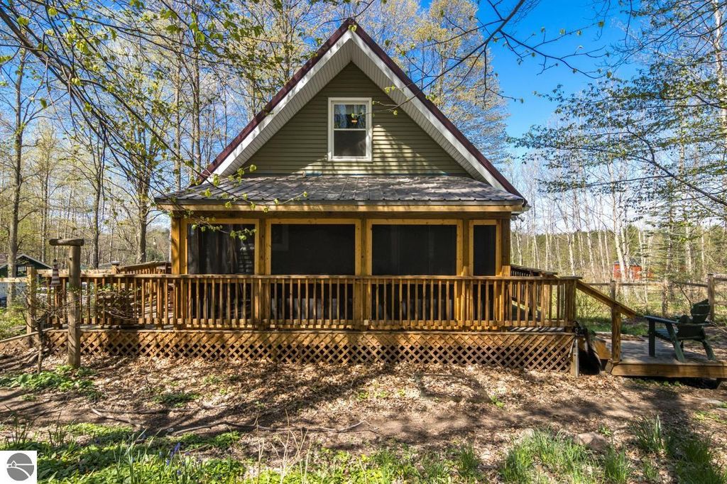 Chalet-style home with a wooden deck surrounded by trees, showcasing a peaceful natural setting on 5 acres near Torch Lake in Alden, MI.
