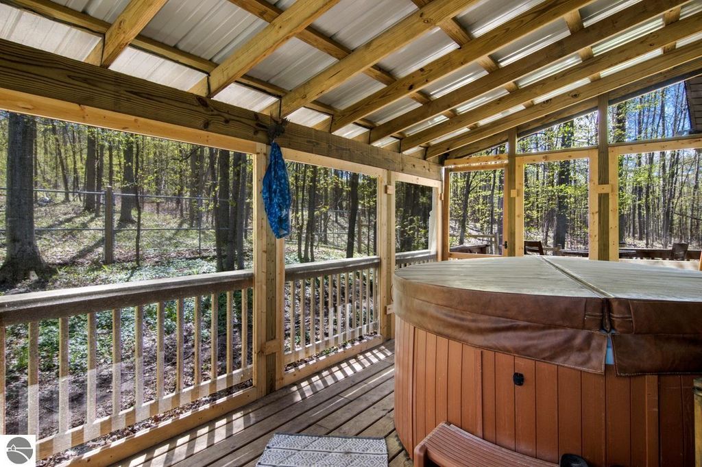 Chalet-style home outdoor deck featuring a hot tub surrounded by trees, highlighting a peaceful natural setting on 5 acres near Torch Lake.