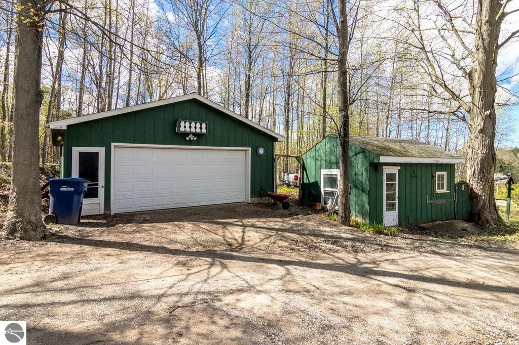 Chalet-style home with green exterior and garage, surrounded by trees on 5 acres in Alden, MI, showcasing a peaceful natural setting near Torch Lake.